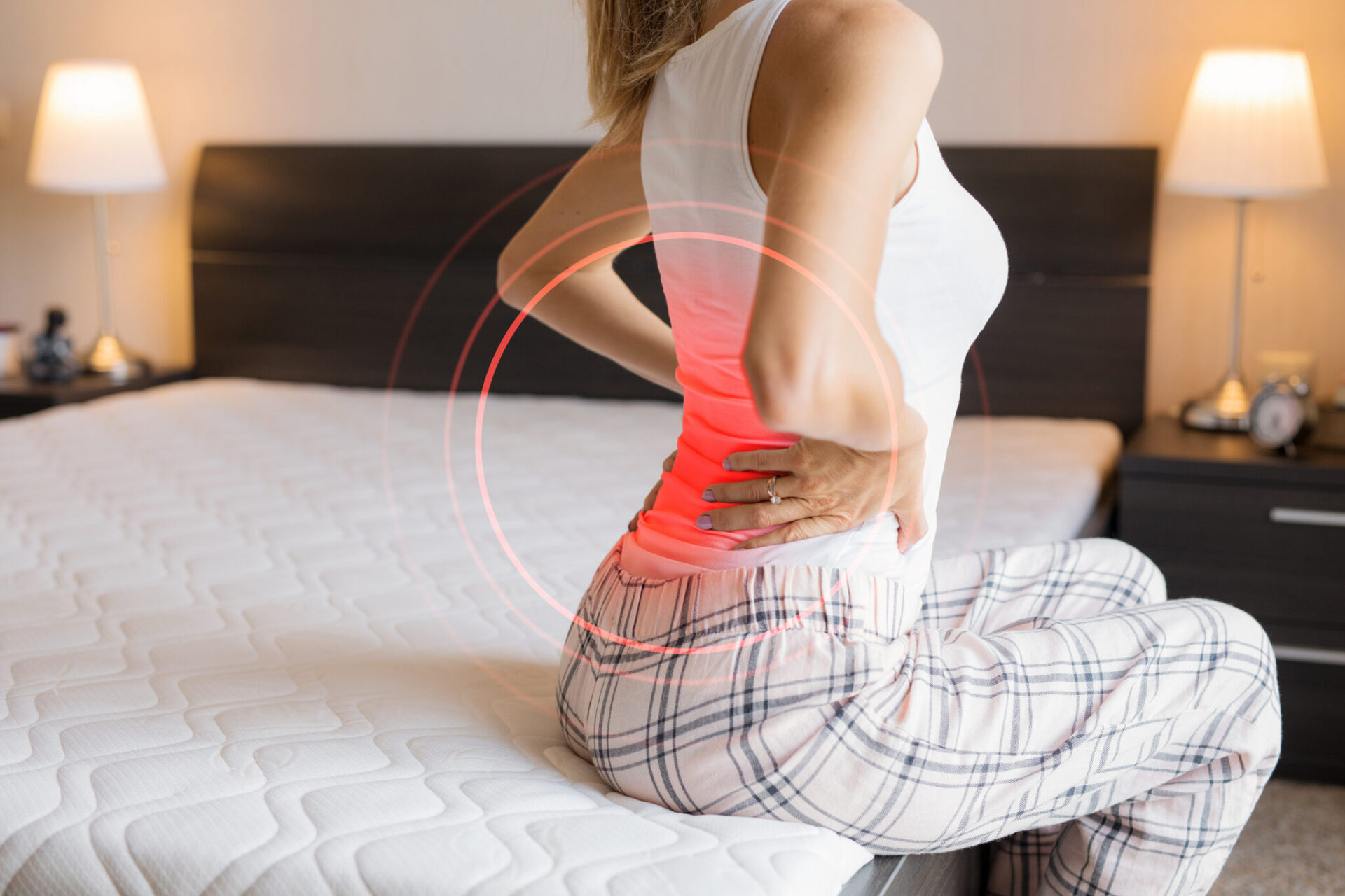 Woman with back pain sitting on bed.