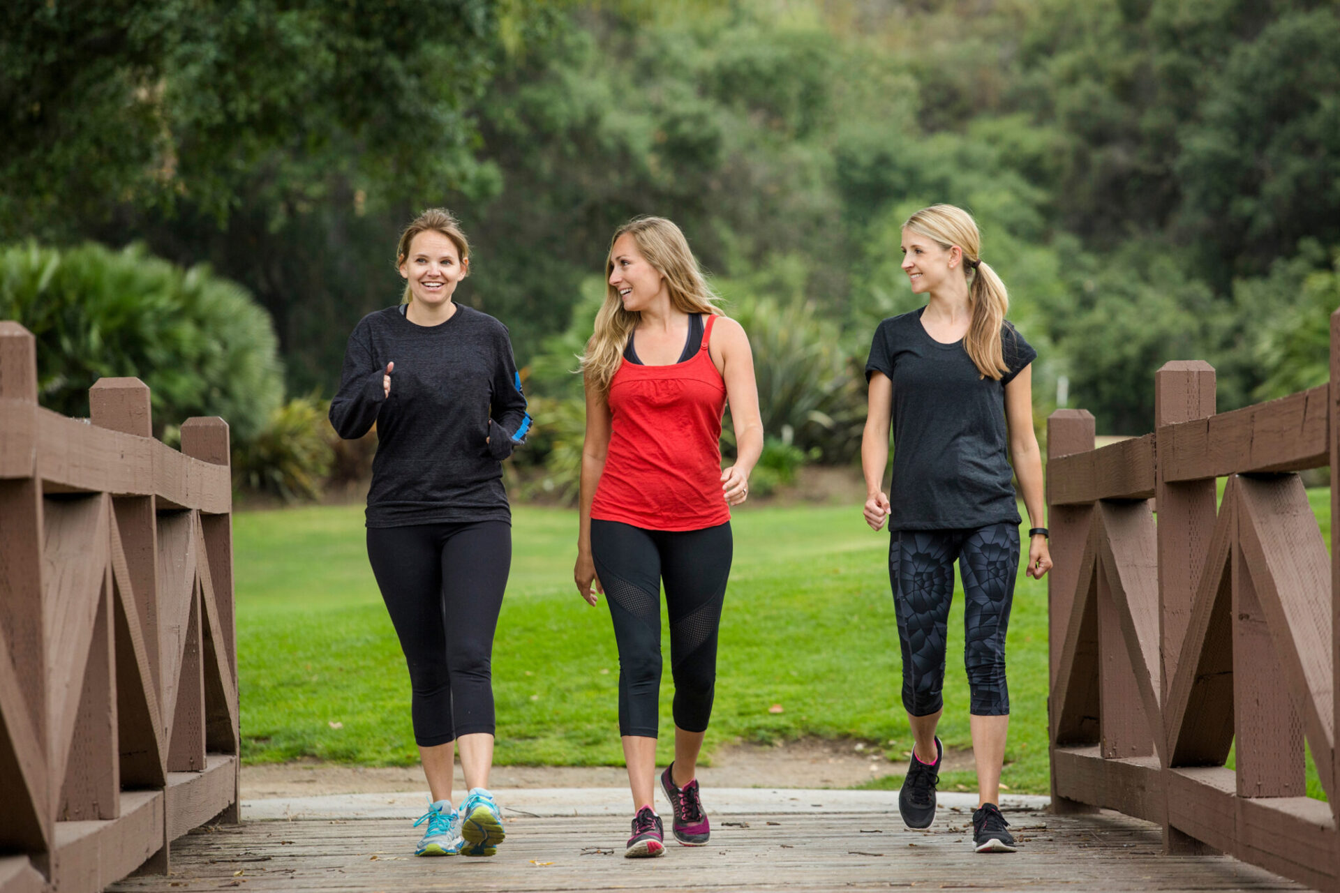 Three women walking on wooden bridge.