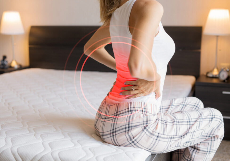 Woman with back pain sitting on bed.