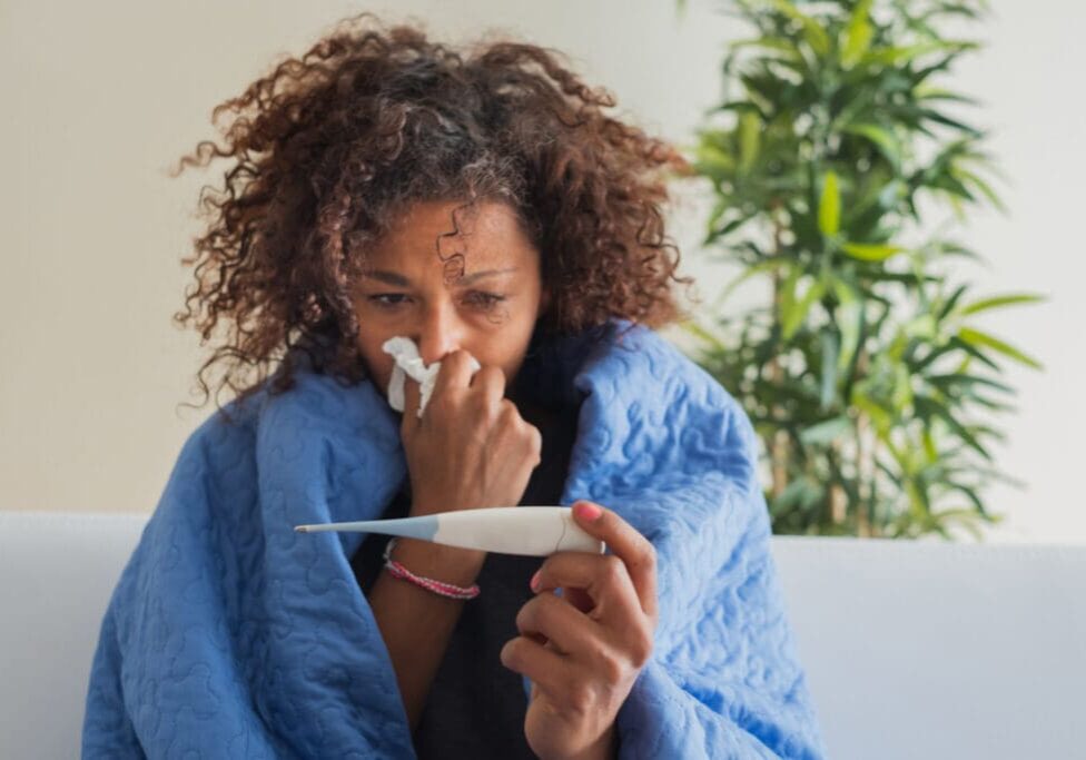 Woman with a cold, holding a thermometer.