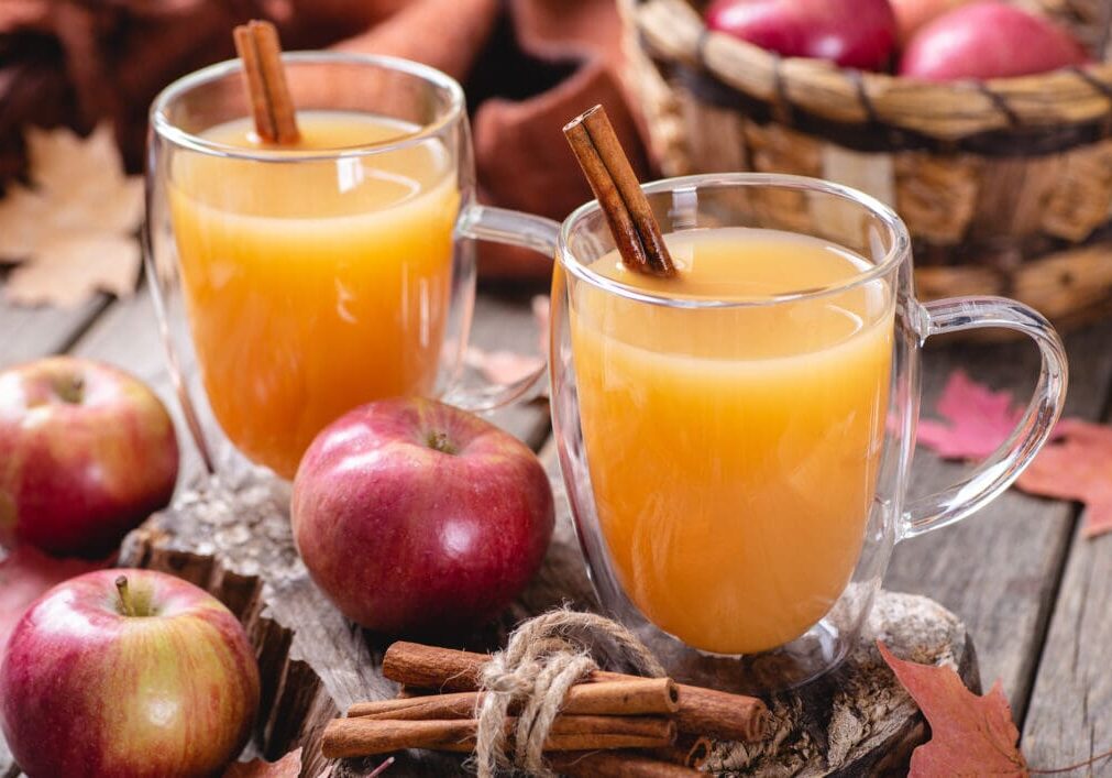 Two mugs of apple cider with cinnamon sticks.