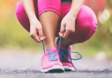 A woman in pink pants tying her shoes.