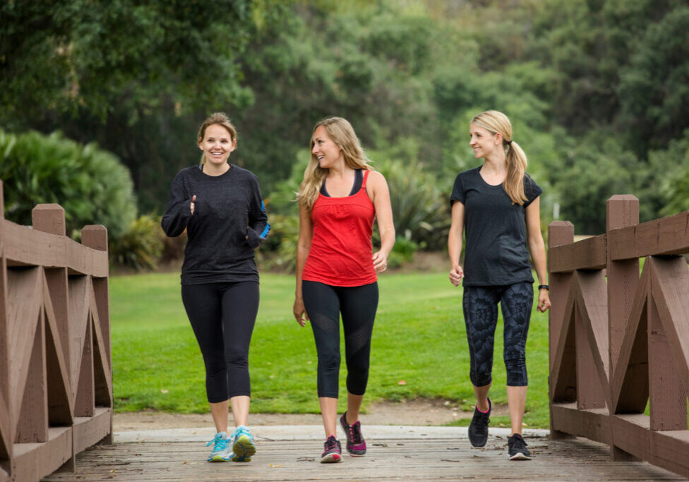 Three women walking on wooden bridge.